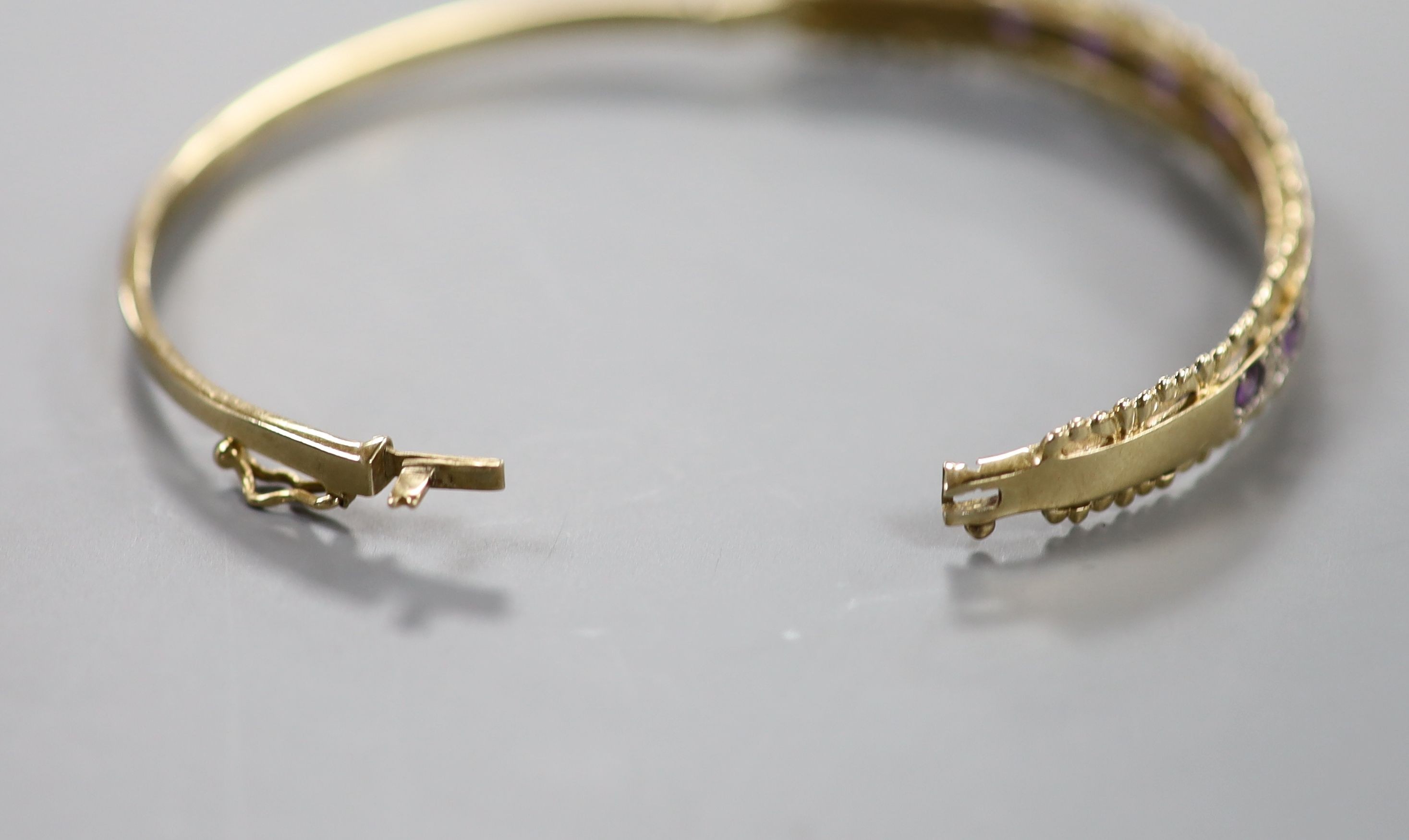 A modern 9ct gold and graduated nine stone amethyst set bracelet, with diamond chip set spacers, interior diameter approx. 56mm, gross 11.3 grams.